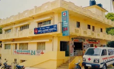 The group's first hospital: the original two-storey Sree Lakshmi Hospital building with its 24-hour signage and an ambulance parked outside