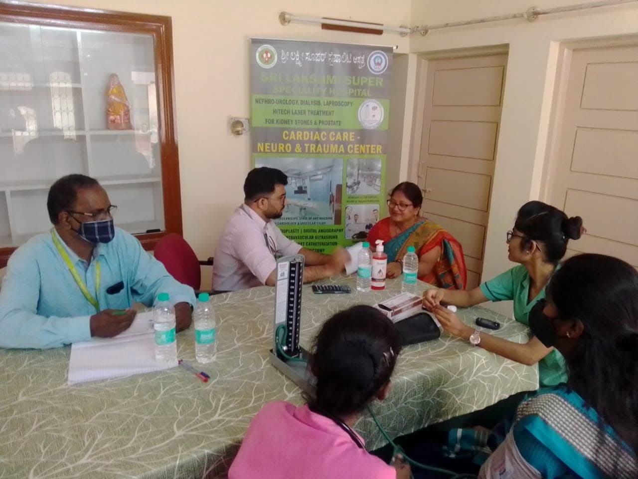 Hospital staff checking a visitor's blood pressure at an indoor health camp consultation.